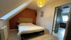 Une chambre avec un plafond en pente, un lit recouvert d’une couvre-lit à motifs géométriques, un radiateur et un luminaire fixé au mur.