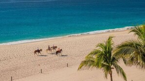 A beach with a clear view of the ocean and a group of people riding horses.