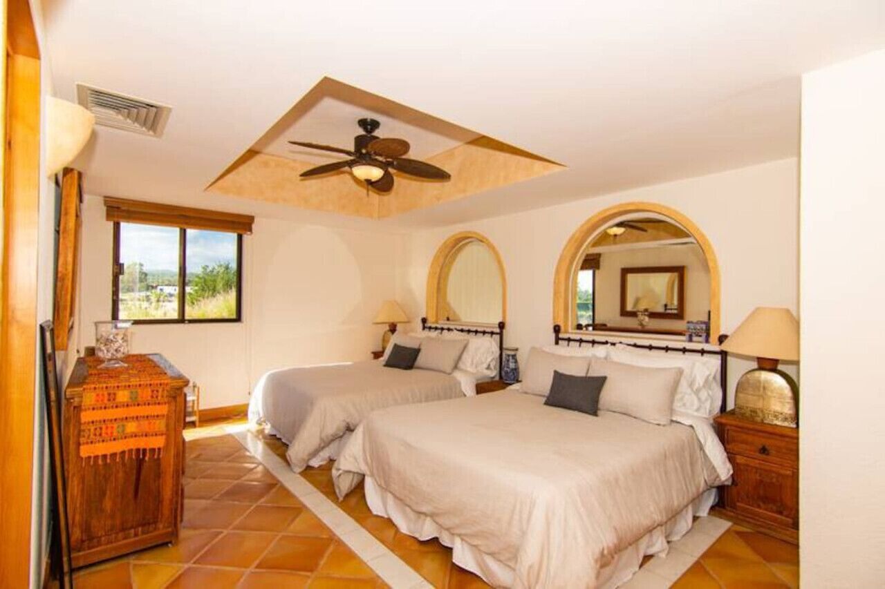 A bedroom with two beds, a ceiling fan, a large window, and a wooden cabinet.