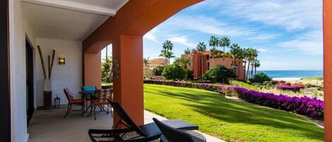 A covered outdoor area with a view of a beach, palm trees, and a well-maintained lawn.