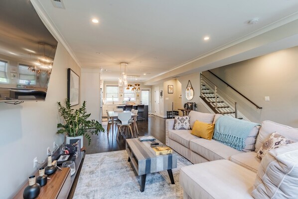 A modern living room with a sofa, coffee table, and a dining area with chairs and a kitchen in the background.