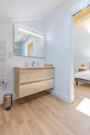 Bathroom features a vanity with a large mirror and a trash bin.