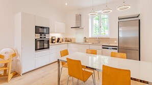 A modern kitchen with white cabinets, stainless steel appliances, a central island with chairs, and pendant lighting. - Le Meix - GIVRY - Gîte (GIVRY)