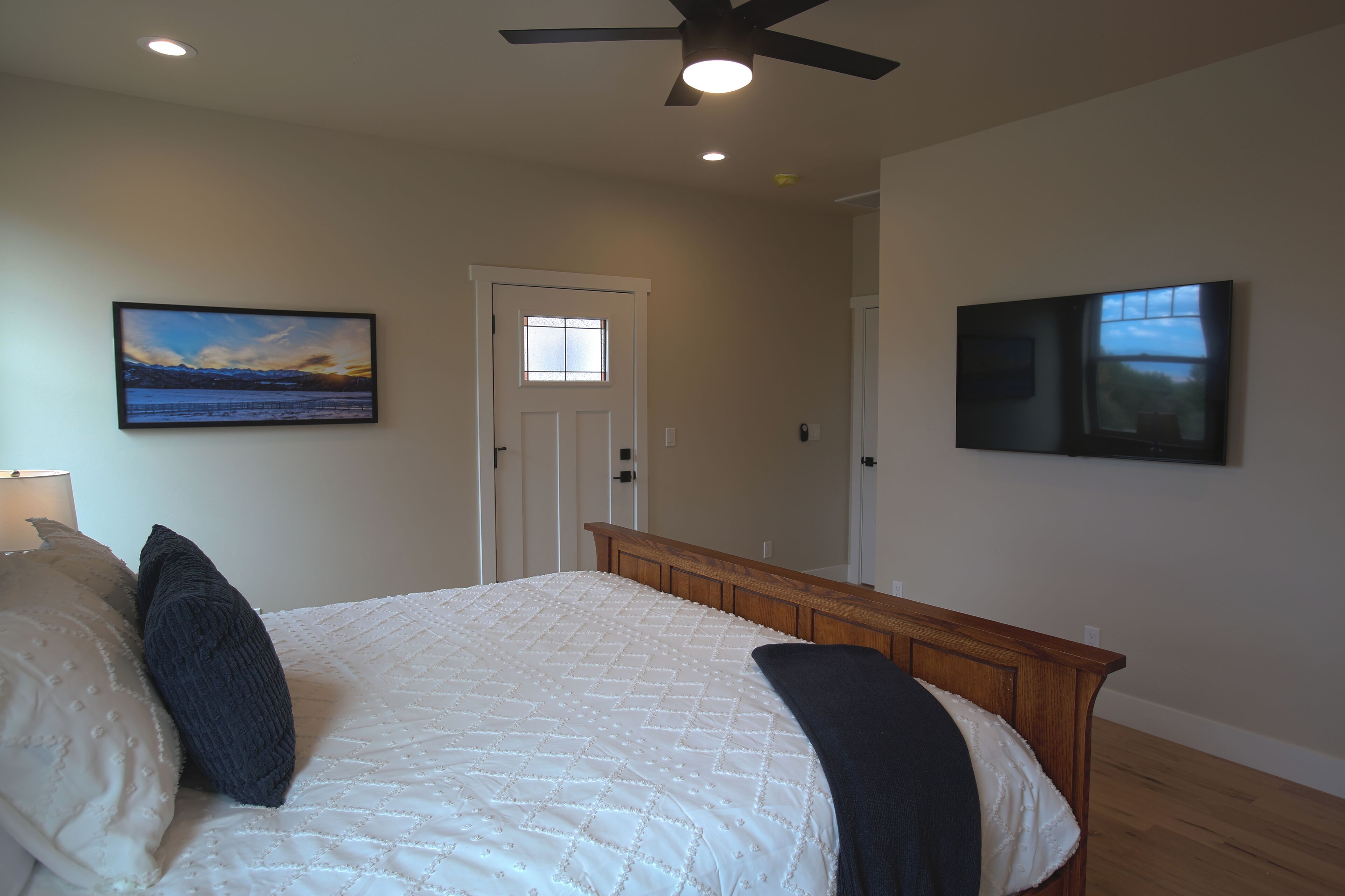 A bedroom with a bed, a ceiling fan, and two wall-mounted paintings.