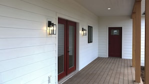 A covered porch with white siding, a red door, and two wall-mounted lights. - New modern farm house on the Still Water Ranch. (Montrose)