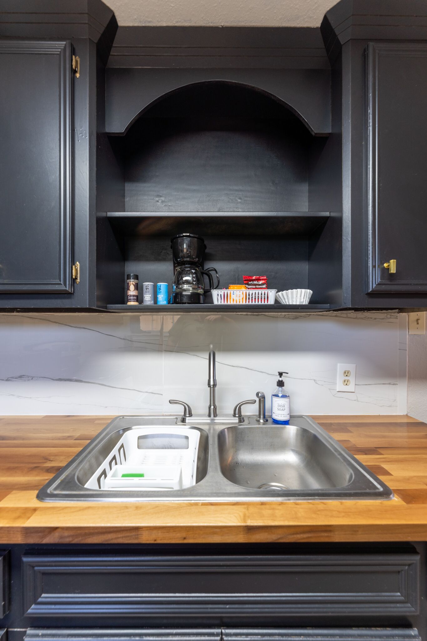 A kitchen with a double sink, dark cabinetry, and a marble countertop.