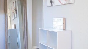 Ein modernes Interieur mit einem weißen Konsolentisch, auf dem ein Willkommensschild steht, einem Spiegel, der ein Bücherregal reflektiert, und einem großen abstrakten Gemälde an der Wand.