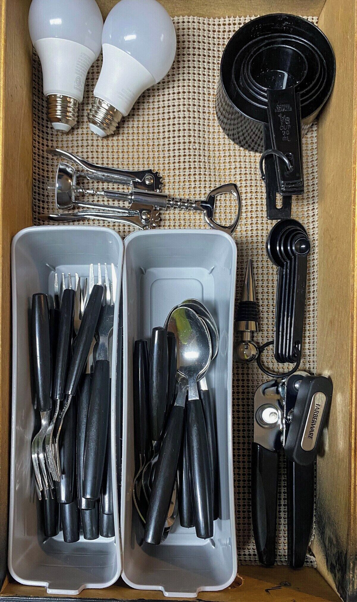 A drawer containing various tools and light bulbs.