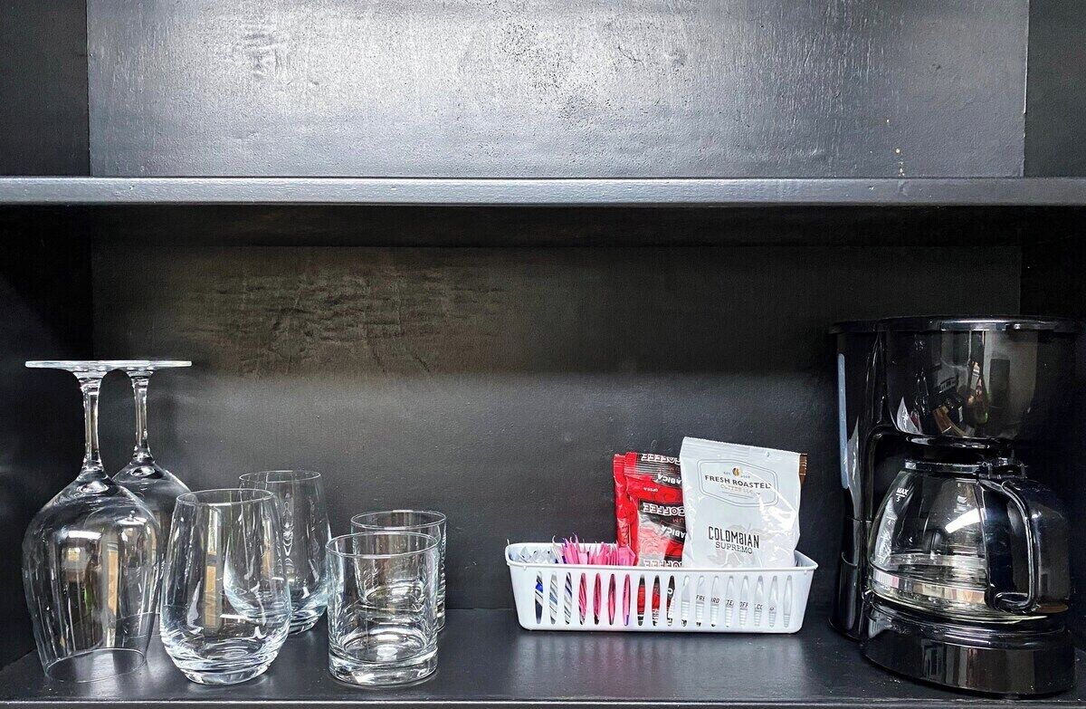 Une étagère avec des verres à vin, une machine à café et des dosettes de café.