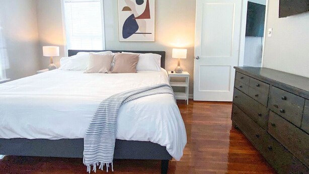 Un dormitorio con cama, lámparas de noche, ventilador de techo, puerta y cómoda.