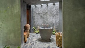 Une salle de bain au sol carrelé, dotée d’une grande baignoire, d’une porte en bois et d’un puits de lumière circulaire.