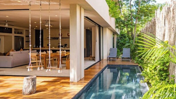 Une maison moderne dotée d’une piscine, de planchers en bois et d’un coin repas avec un canapé et des fauteuils.