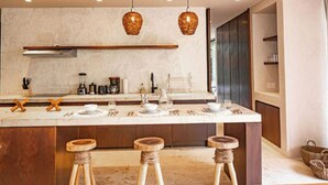 Une cuisine moderne dotée d’un plan de travail en marbre, de tabourets en bois, de luminaires suspendus en osier et d’un four encastré.
