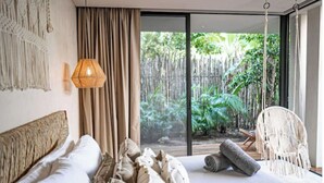 Une chambre avec un grand lit, un luminaire suspendu et une vue sur un jardin tropical, visible à travers une porte-fenêtre coulissante.