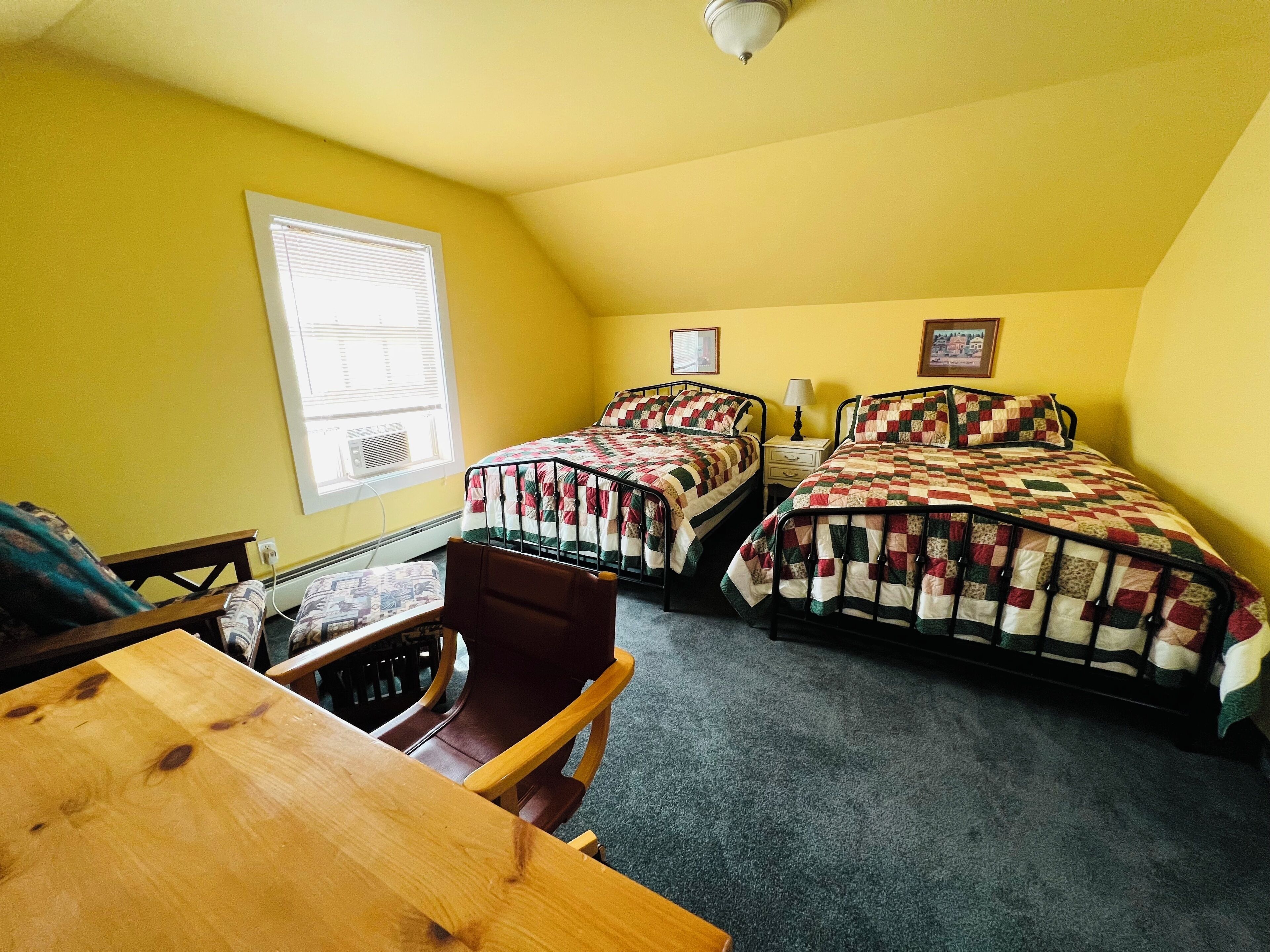 A room with two beds, a wooden table, and a chair.