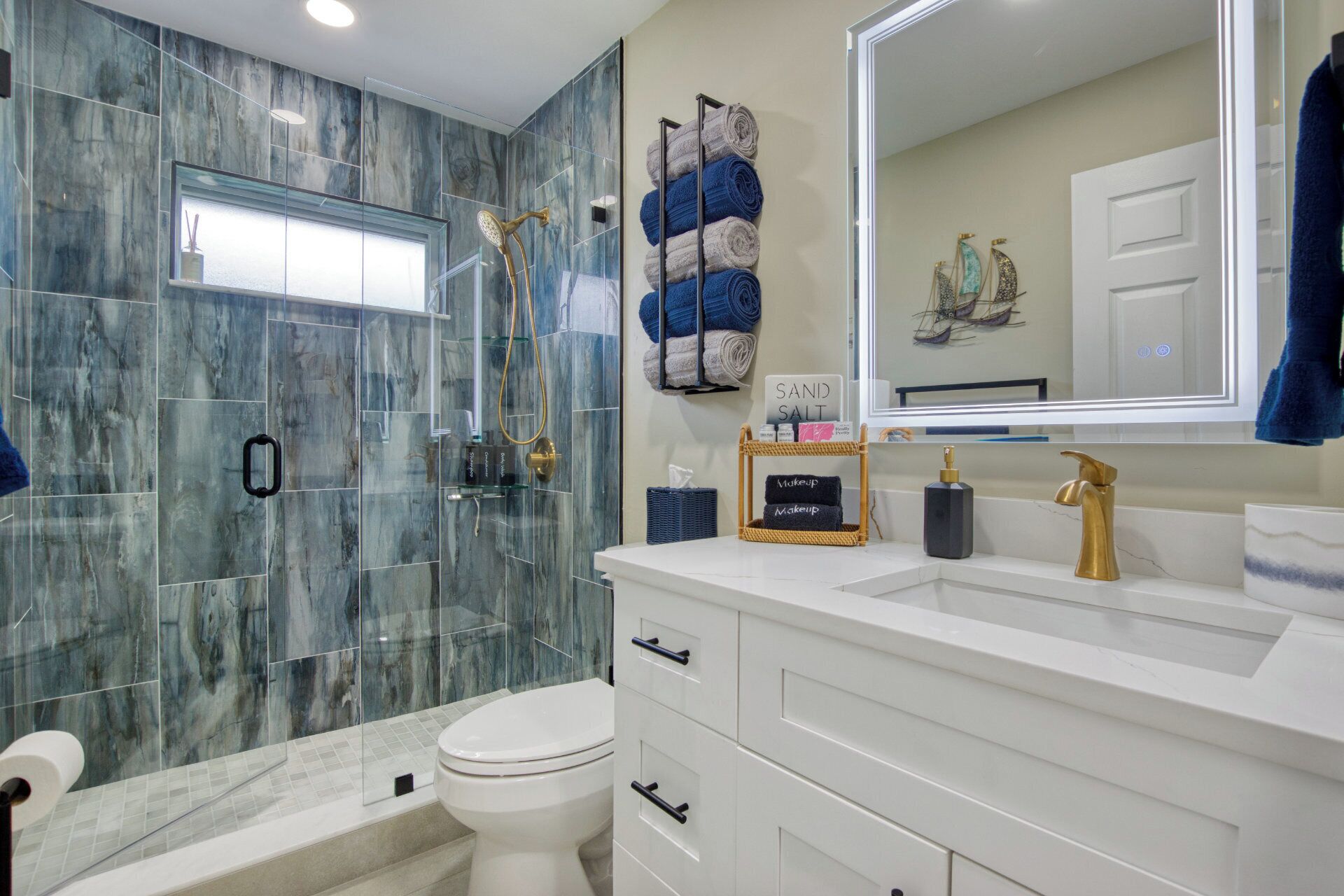 Une salle de bain dotée d’une douche à parois de verre, d’un meuble-lavabo blanc avec des accessoires dorés et d’un grand miroir.