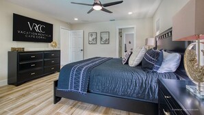 Une chambre à coucher moderne avec un lit, un ventilateur de plafond, un téléviseur fixé au mur et une commode.
