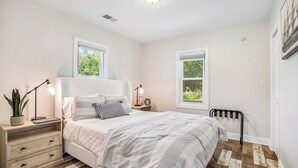 A bedroom with a bed, nightstands, a lamp, a potted plant, and a window.