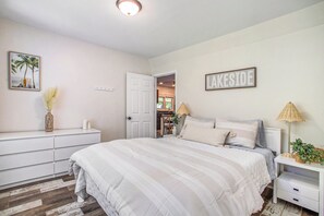 Une chambre à coucher comprenant un lit, des tables de chevet, une commode et une porte donnant sur une autre pièce.