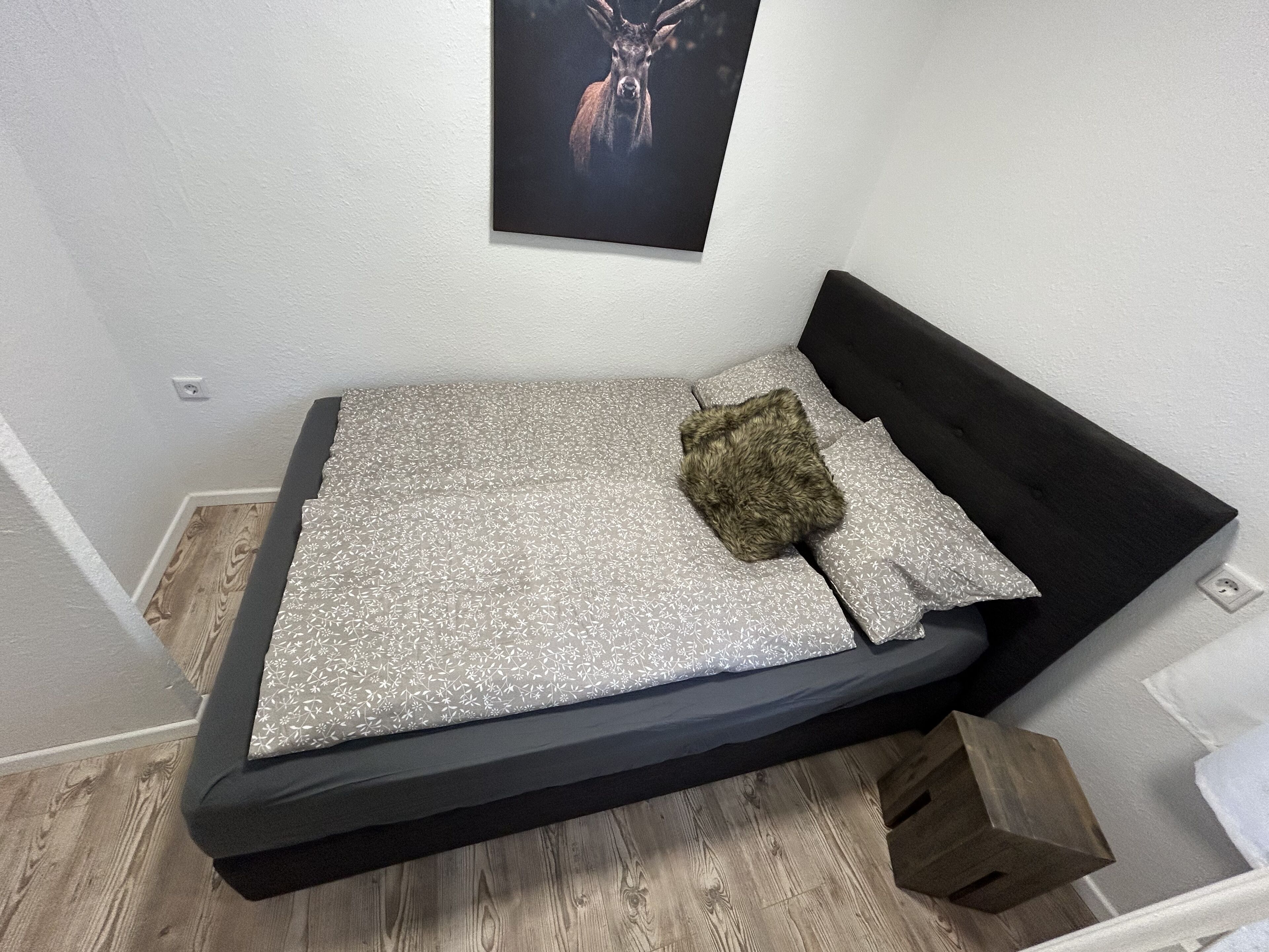 Un petit lit de couleur sombre, recouvert d’une couvre-lit à motifs et agrémenté d’un seul oreiller.