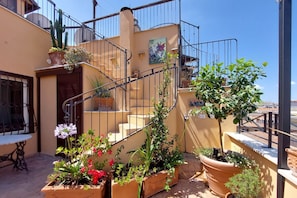 A rooftop terrace with potted plants, a staircase, and a mural.
