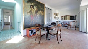 Un comedor con un cuadro grande, sillas de madera, una mesa y una estantería.