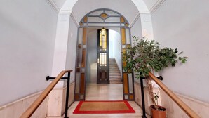 Una escalera con alfombra roja, una planta en maceta y una puerta con lámpara.