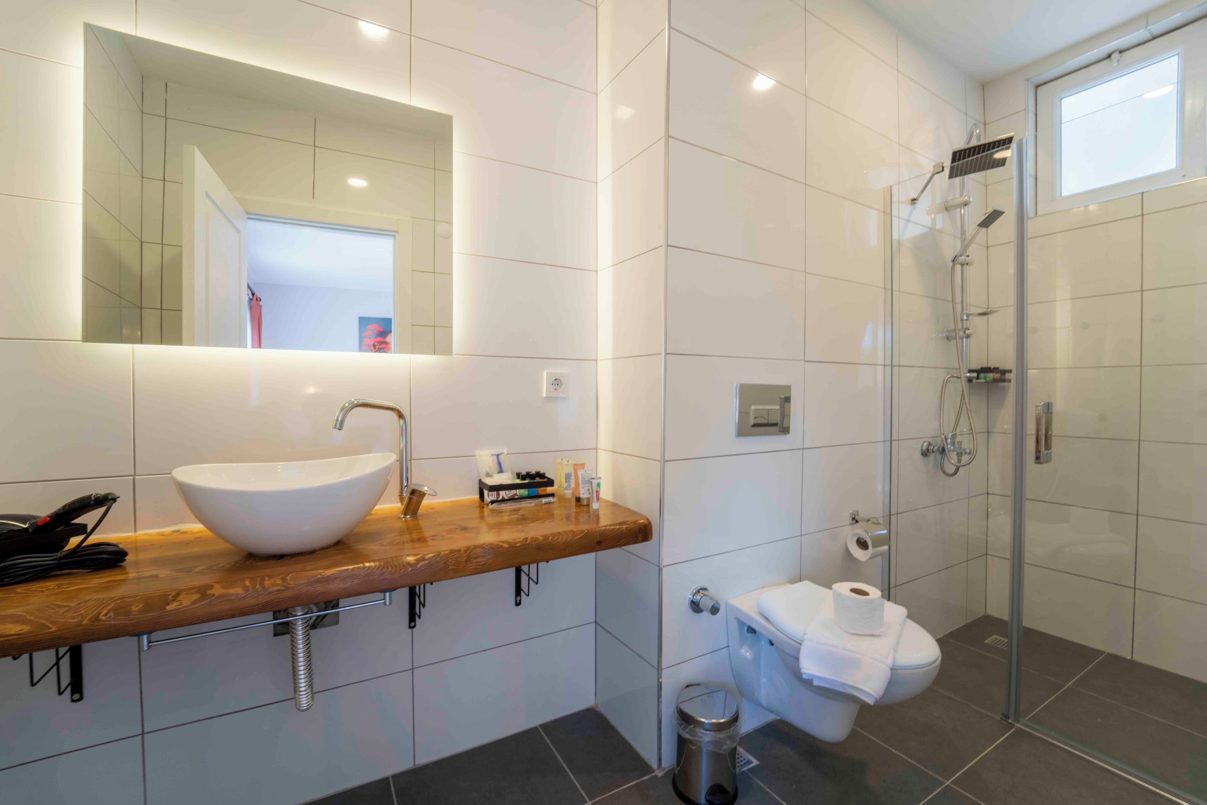 Un baño moderno con un espejo grande, un lavabo sobre encimera, una ducha y un inodoro.