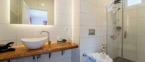 Un baño moderno con un espejo grande, un lavabo sobre encimera, una ducha y un inodoro.