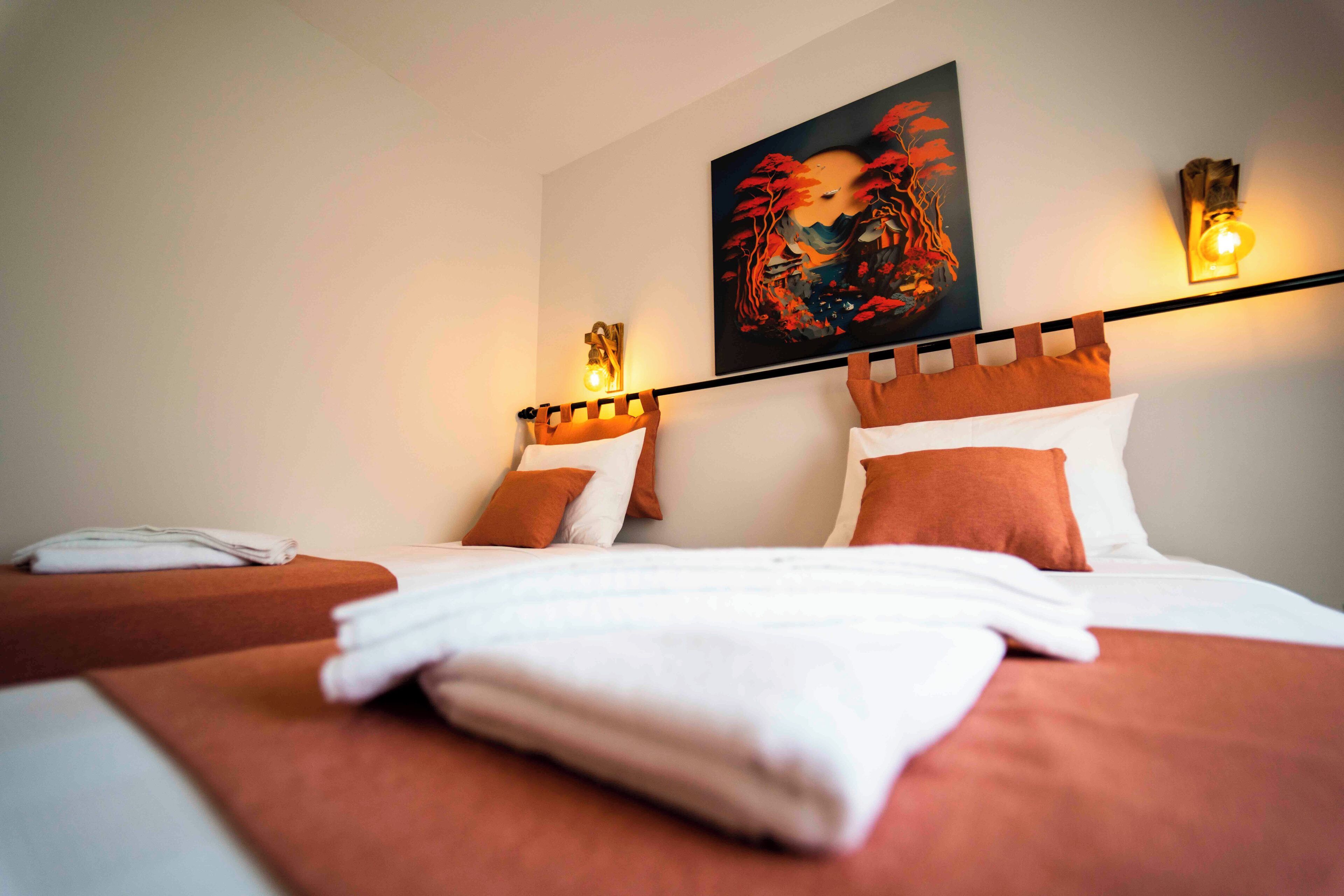 A hotel room with a bed, pillows, a folded towel, and a painting on the wall.