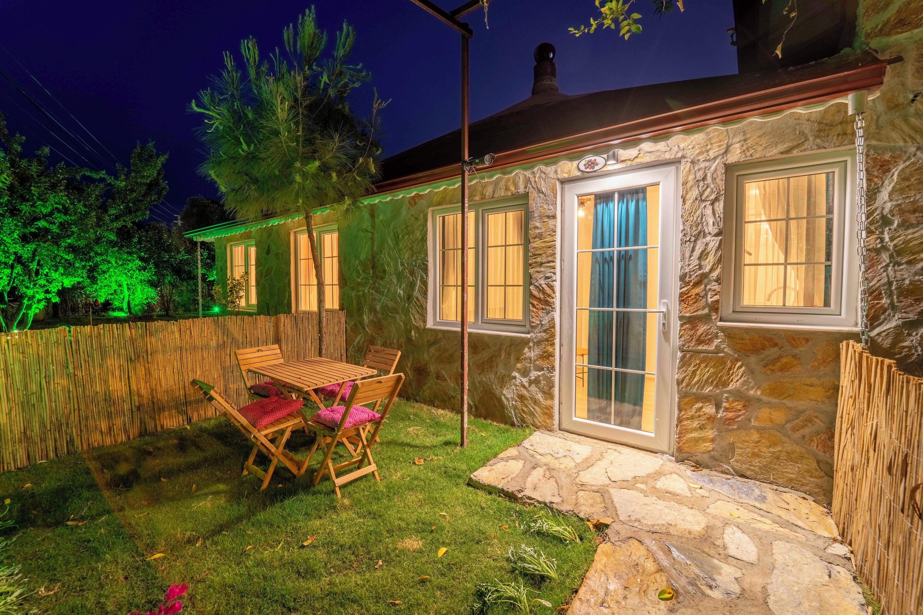 A stone house with a patio, a wooden table, and chairs.