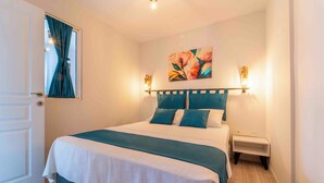 Una cama bien hecha con un edredón verde azulado y blanco, dos almohadas a juego y una mesita de noche con una lámpara.