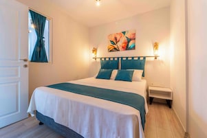 Una cama bien hecha con un edredón verde azulado y blanco, dos almohadas a juego y una mesita de noche con una lámpara.
