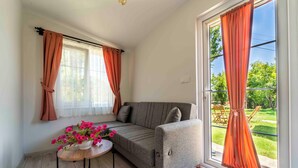 Una habitación acogedora con un sofá, una mesita con flores y ventanas amplias con cortinas.