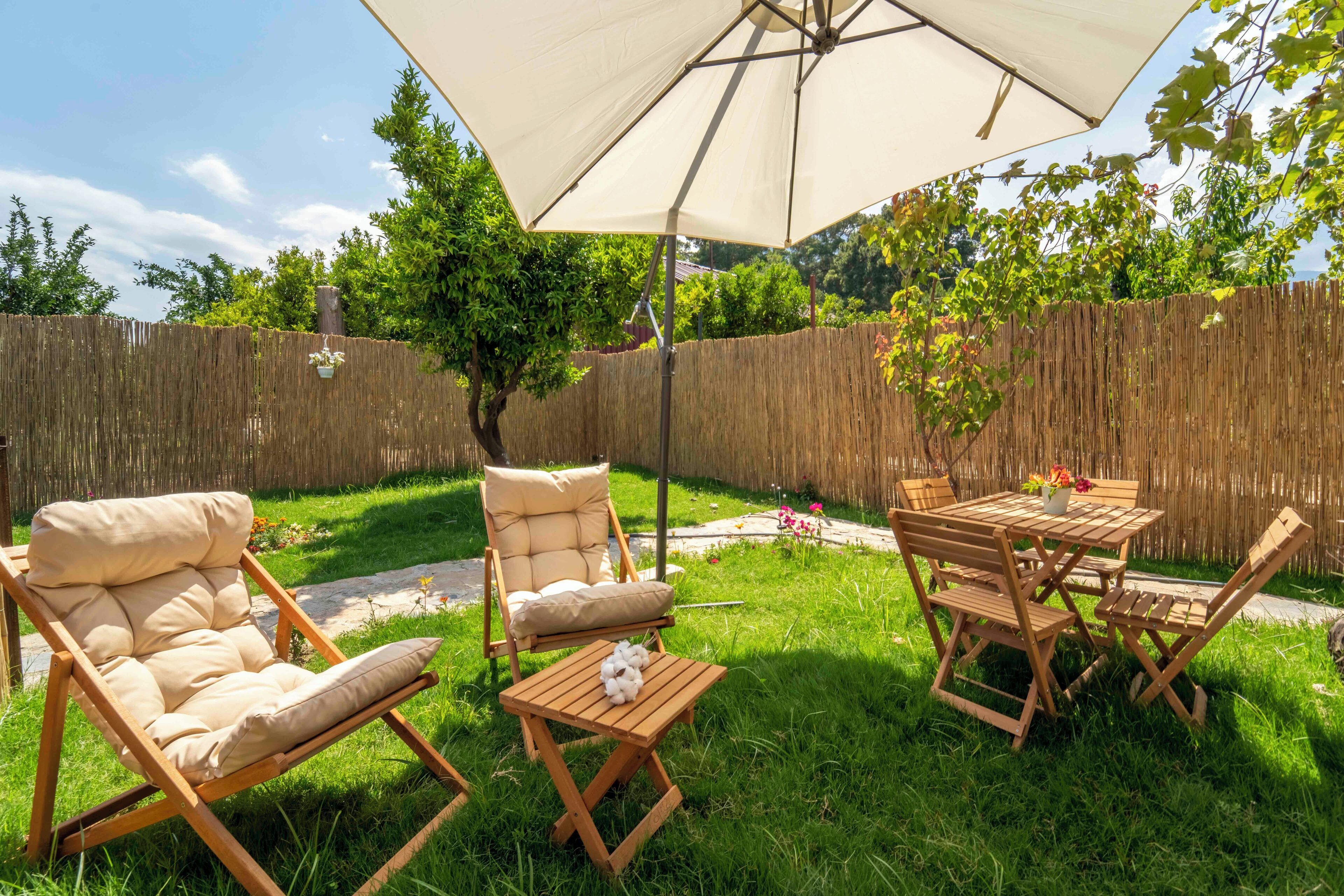 An outdoor patio with a wooden table and chairs, a cushioned lounge chair, and a large umbrella.