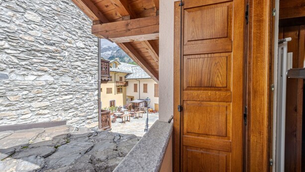 Un mur de pierre, une porte en bois et une vue sur une cour intérieure avec des bâtiments.