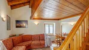 Un salon avec un plafond en bois, un canapé incurvé, une table à manger avec des chaises et un escalier.