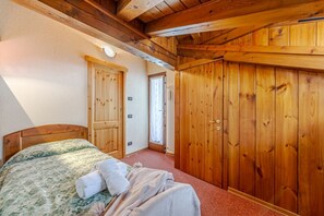 Une chambre avec un plafond en bois, un lit recouvert d’une couvre-lit à motifs floraux et une armoire en bois.