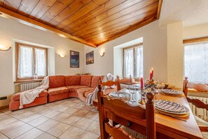Un salon chaleureux avec un plafond en bois, un canapé, une table à manger avec des chaises et une cheminée.