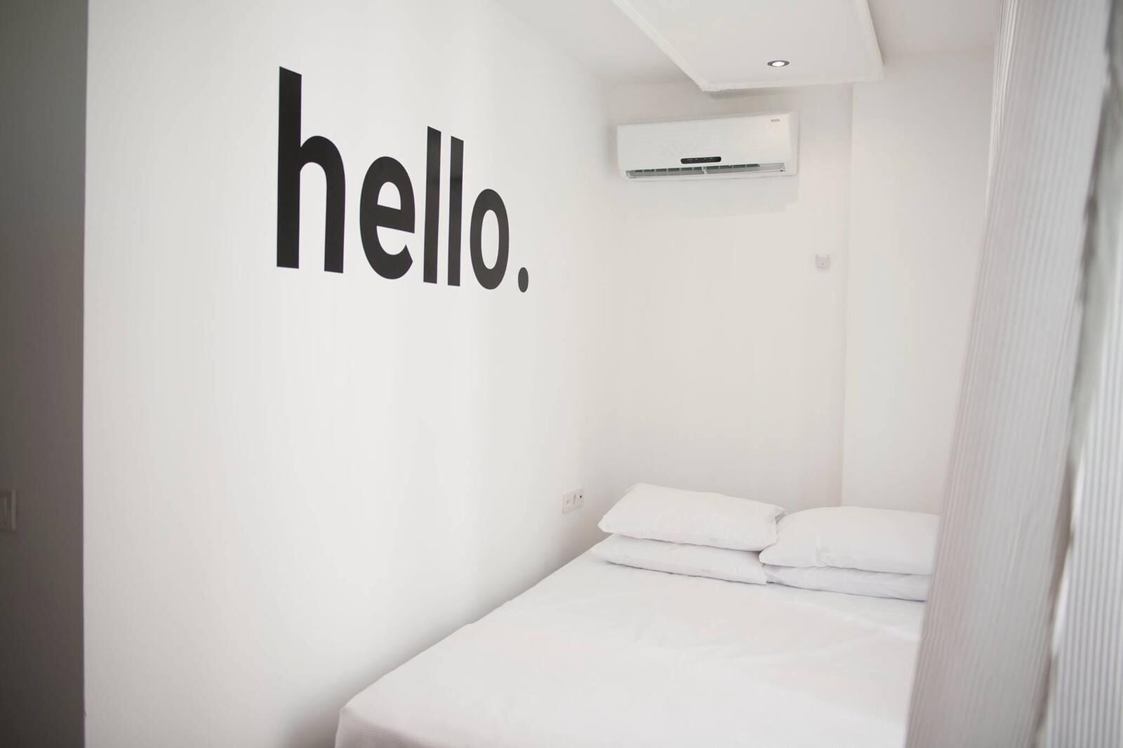 Une chambre à coucher minimaliste avec un lit, des murs blancs et un grand mot écrit : « Bonjour ».