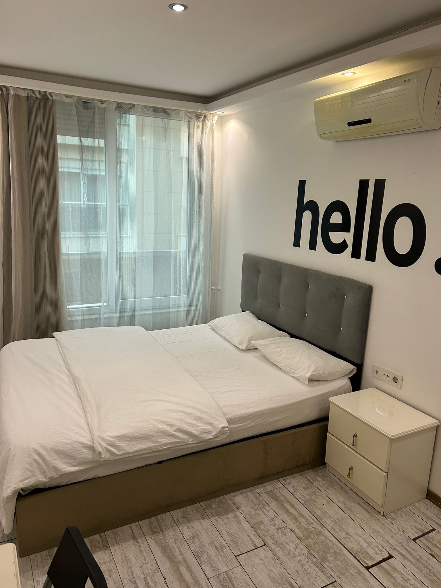 A modern bedroom with a large bed, a bedside table, a nightstand, and a wall-mounted air conditioner.