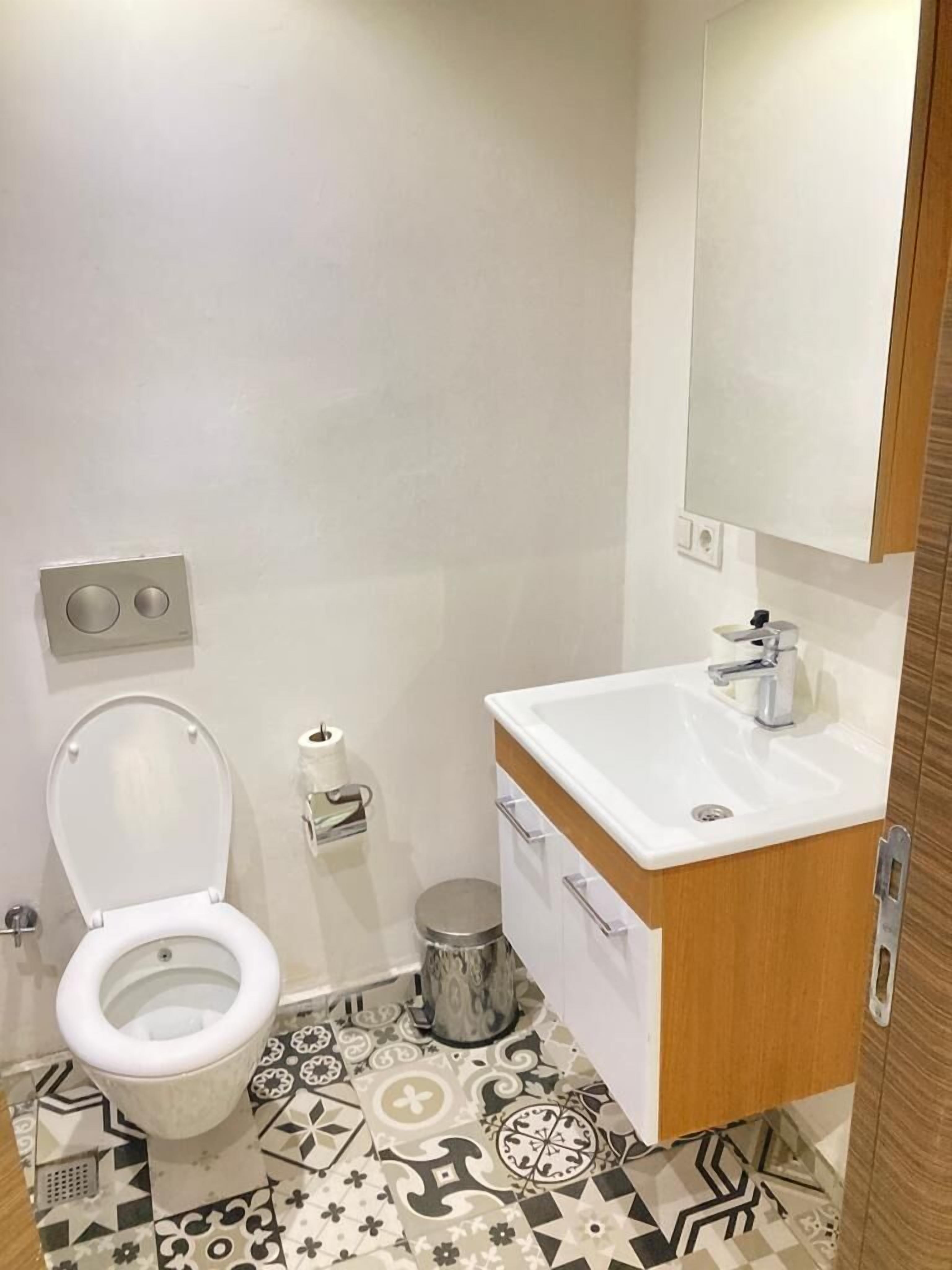 A bathroom with a toilet, sink, mirror, and patterned floor tiles.