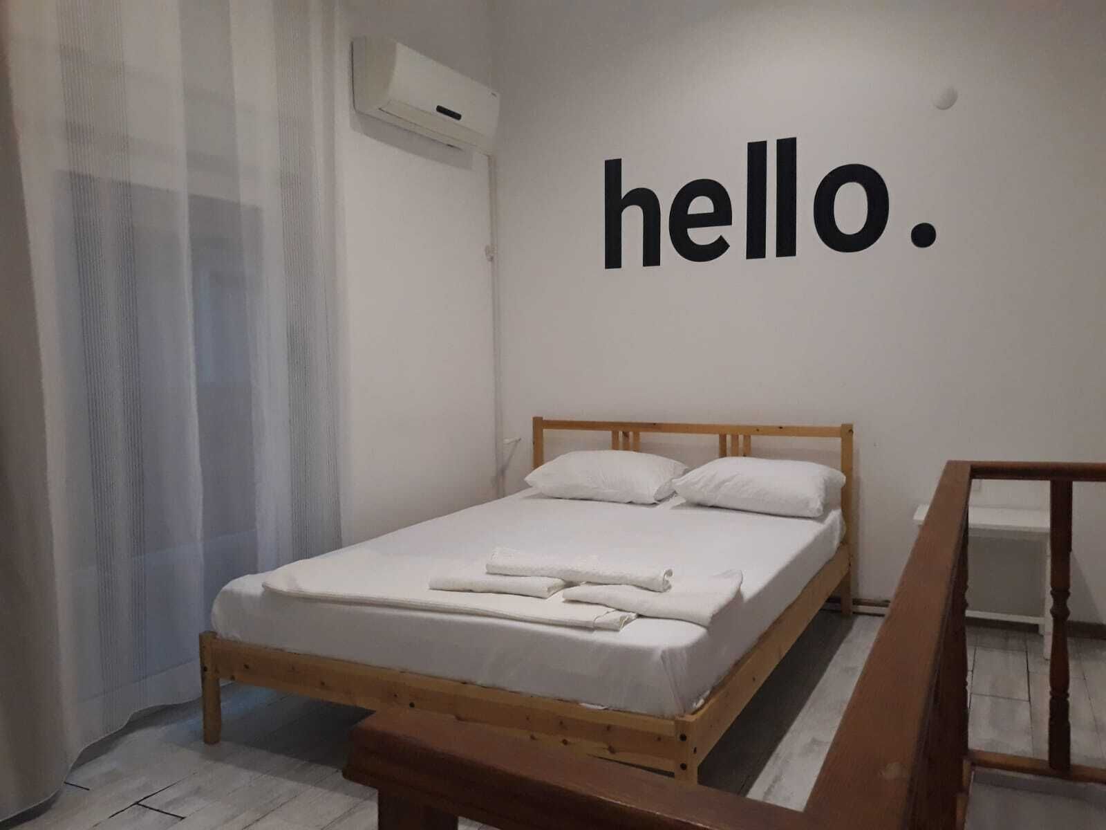 A simple bedroom with a bed, a bench, a wall-mounted air conditioner, and a 'hello.' sign.