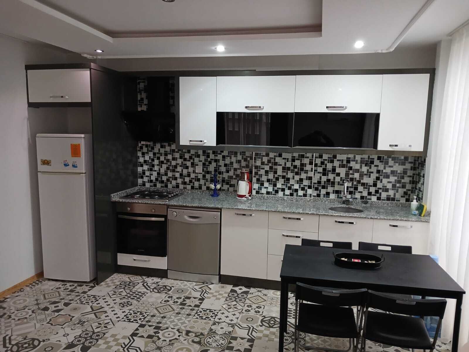 A compact kitchen with white cabinets, a tiled backsplash, a gas stove, a dishwasher, and a dining table with chairs.