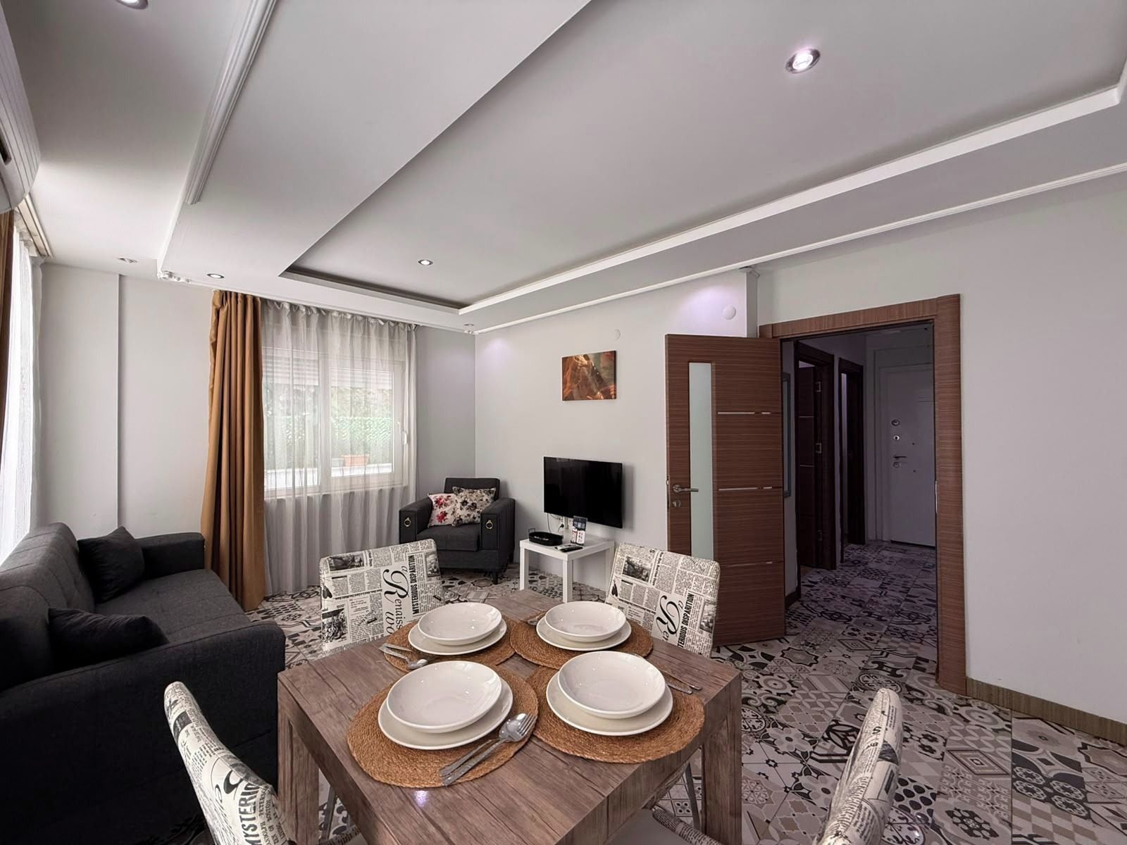 A modern living room with a sofa, a dining table set with plates, a television, and a patterned floor.