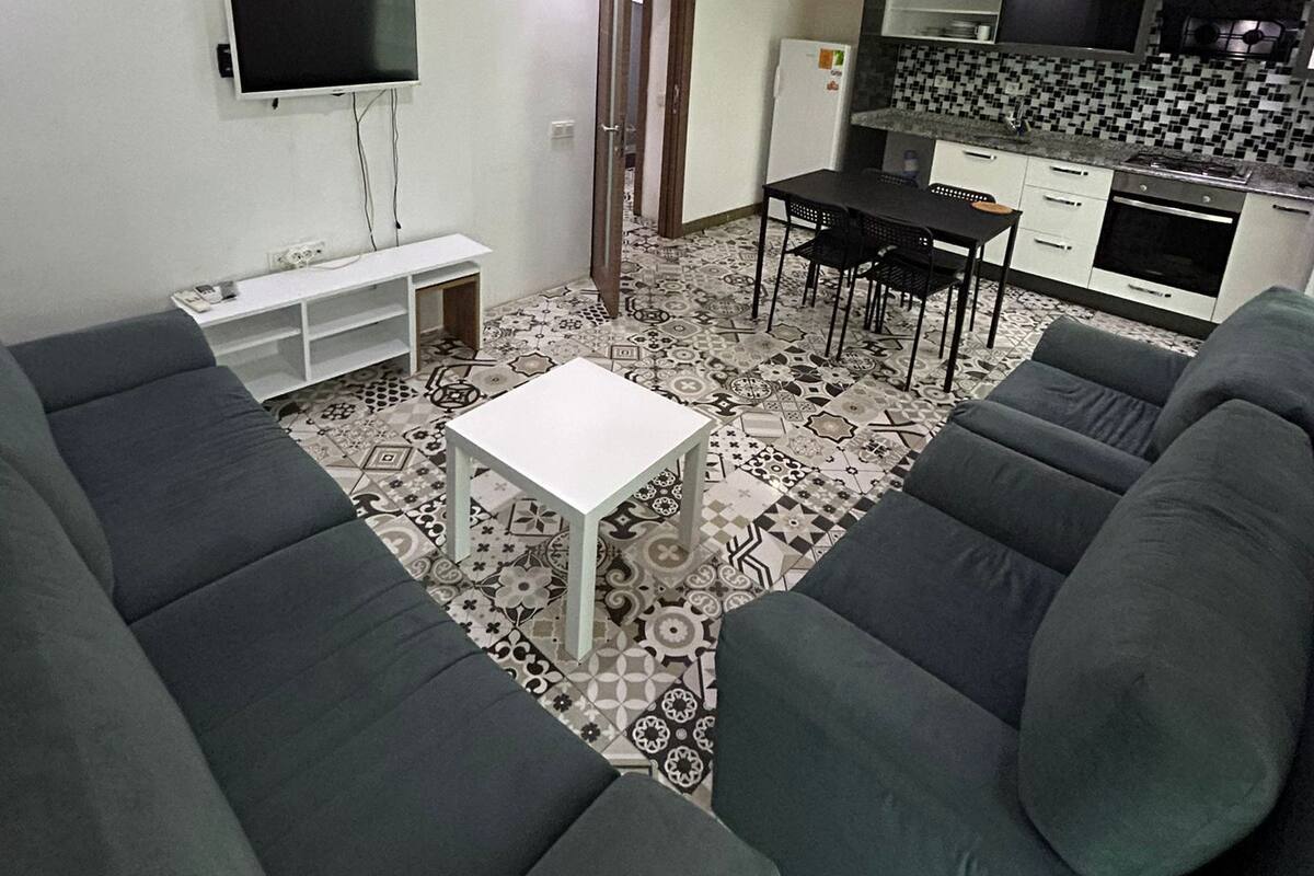 Ein kompakter Wohnraum mit Sofa, Fernseher, Küchenzeile und strukturiertem Boden.