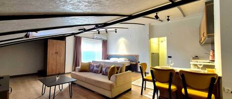 A compact living space with a sofa, dining table, and chairs, a kitchenette, and a bed with a window.