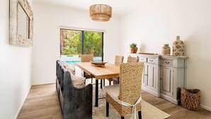 A dining area with a wooden table, woven chairs, a hanging light fixture, and a view of a pool through a window. - NEW! Serenity & Style in Sedona - Pool, Red Rock Views, & more! (Sedona)