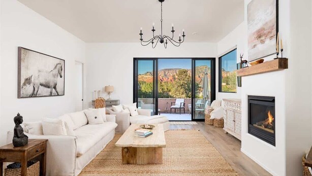 A spacious living room with a white sofa, a wooden coffee table, a fireplace, and a large window with a mountain view. - NEW! Serenity & Style in Sedona - Pool, Red Rock Views, & more! (Sedona)