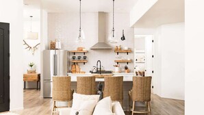 A modern kitchen with a central island, hanging pendant lights, and a dining area with wicker chairs. - NEW! Serenity & Style in Sedona - Pool, Red Rock Views, & more! (Sedona)
